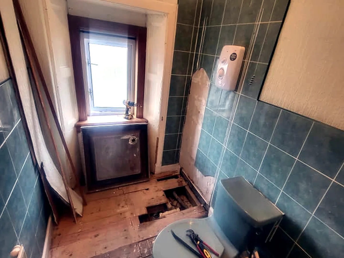 Bathroom before renovation, stripped to bare floorboards